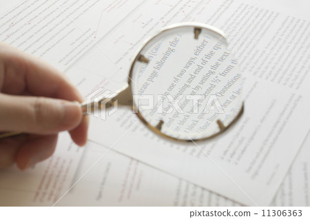 Hand holding magnifying glass to read document 11306363