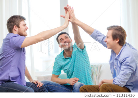 smiling male friends giving high five at home 11311430
