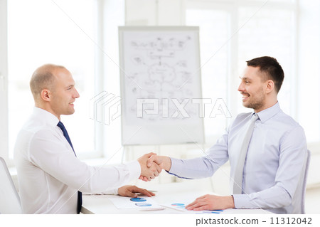 two smiling businessmen shaking hands in office 11312042