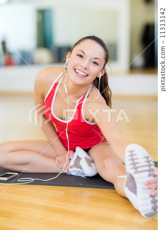 smiling girl with smartphone and earphones in gym 11313142