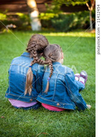 little sisters sitting on grass head to head with joint braids little sisters sitting on grass head to head with joint braids 11412454