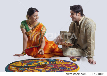 Maharashtrian couple placing diyas on rangoli 11454005