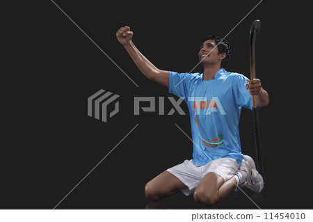 Happy young hockey player with stick celebrating success over black background Happy young hockey player with stick celebrating success over black background 11454010