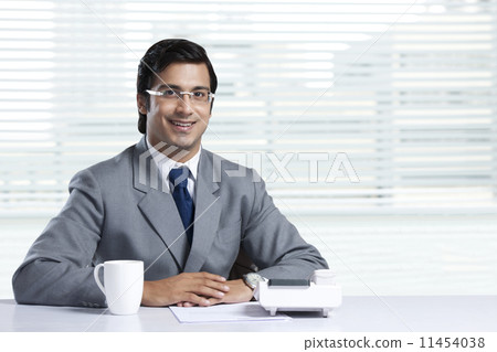 Portrait of confident businessman sitting at desk in office 11454038