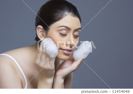 Beautiful young woman washing face with soap sud over blue background Beautiful young woman washing face with soap sud over blue background 11454046
