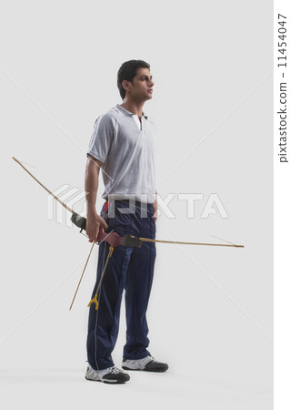 Young male archer standing with bow and arrow isolated over gray background 11454047