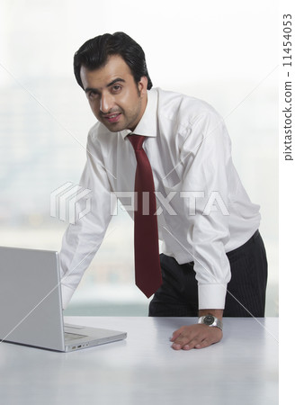 Portrait of young businessman with laptop at office desk 11454053