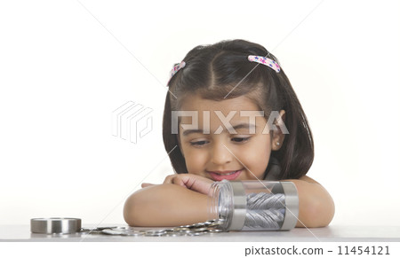 Girl looking at Indian coins spilled on table against white background 11454121