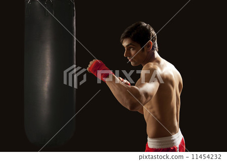 Side view of young man hitting punching bag isolated over black background 11454232