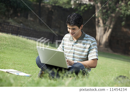Student with a laptop sitting in a park 11454234