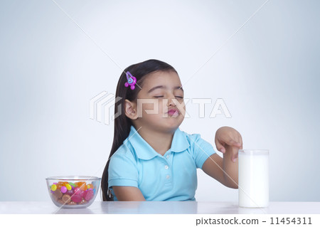 Cute girl choosing between milk and bowl of sweet food against blue background 11454311