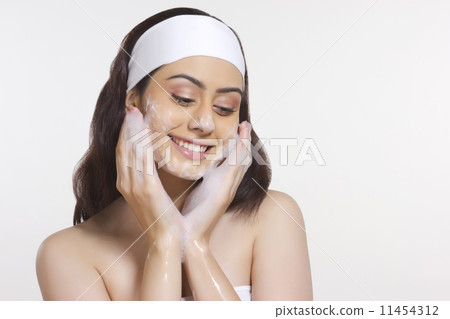Smiling woman applying soap on face against white background 11454312