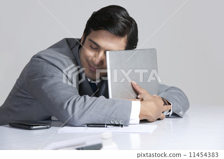 Loving businessman embracing laptop at desk over gray background 11454383