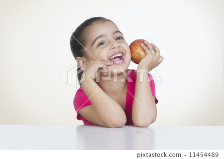 Cheerful girl holding fresh red apple against colored background Cheerful girl holding fresh red apple against colored background 11454489