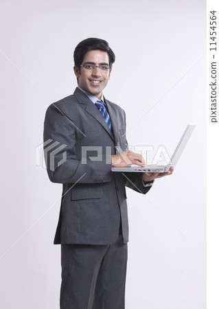 Portrait of smiling businessman using laptop over gray background 11454564