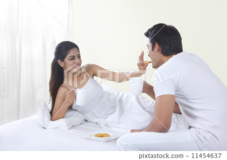 Happy young woman feeding biscuit to man in bed Happy young woman feeding biscuit to man in bed 11454637