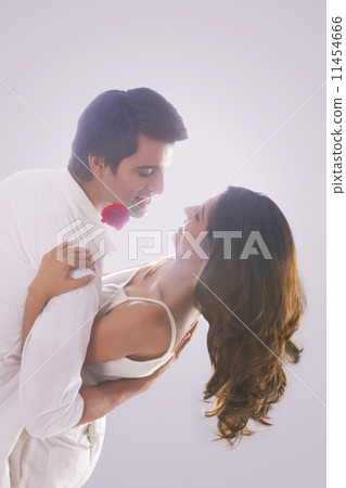Romantic young man holding red rose in mouth while dancing with woman over white background 11454666