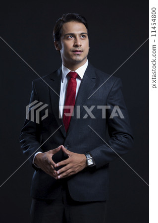 Thoughtful businessman with hands clasped standing against black background 11454800