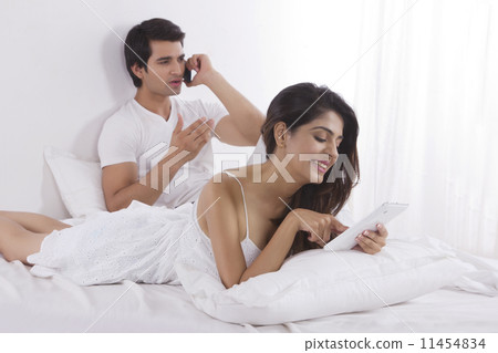 Happy young woman using digital tablet with man on call in bedroom Happy young woman using digital tablet with man on call in bedroom 11454834