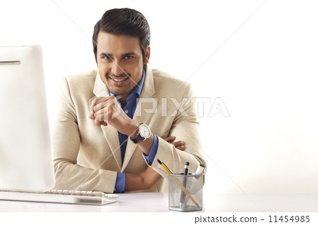 Portrait of confident young businessman sitting at computer desk 11454985