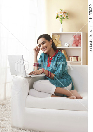 Full length of young Indian woman using laptop on sofa at home 11455029