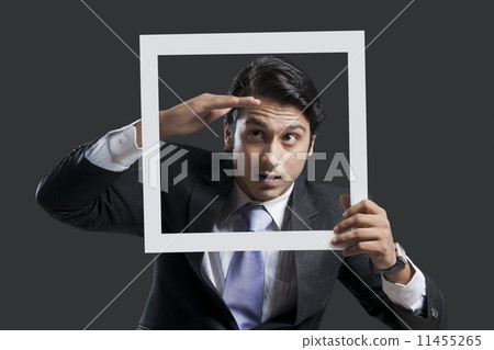 Young businessman shielding eyes while holding frame over black background 11455265
