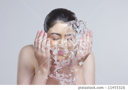 Beautiful woman washing face with water over gray background 11455328