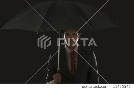 Portrait of confident businessman holding umbrella against black background 11455545