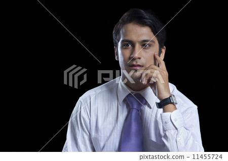 Thoughtful young businessman with hand on chin over black background 11455724