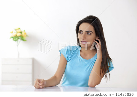 Thoughtful young woman sitting at table in house Thoughtful young woman sitting at table in house 11455826