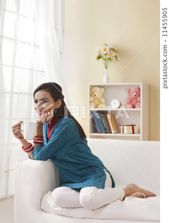 Full length of beautiful Indian woman having coffee on sofa 11455905
