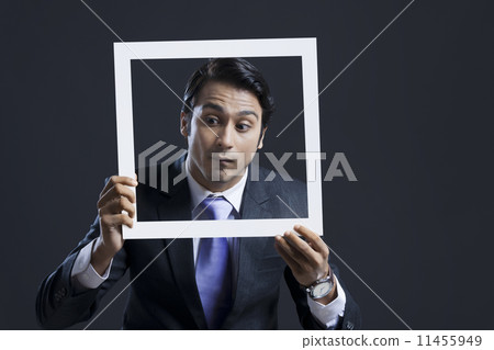 Businessman looking down while holding picture frame against black background 11455949