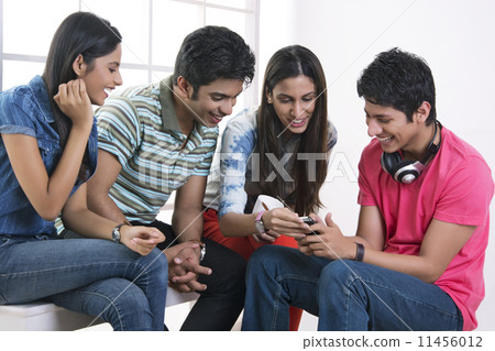 Happy friends looking at mobile phone in college 11456012