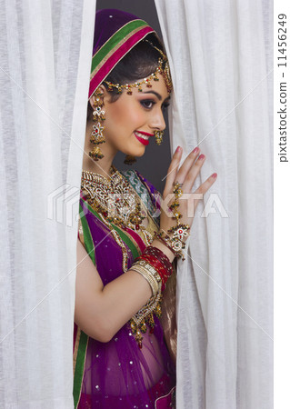Shy Indian bride standing amidst curtains 11456249