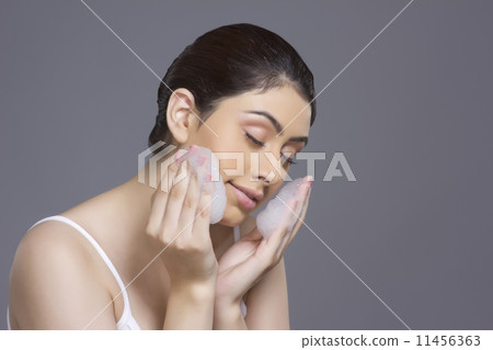 Beautiful woman applying soap sud on face against gray background 11456363