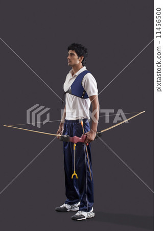 Full length of young male archer with bow and arrow over gray background Full length of young male archer with bow and arrow over gray background 11456500