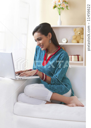 Happy Indian woman using laptop on sofa 11456622