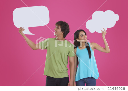 Thoughtful young couple holding communication bubbles against pink background Thoughtful young couple holding communication bubbles against pink background 11456926
