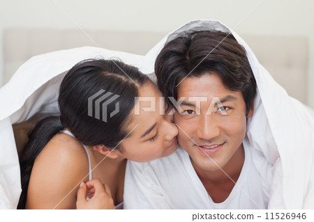 Happy couple lying on bed together under the duvet Happy couple lying on bed together under the duvet 11526946