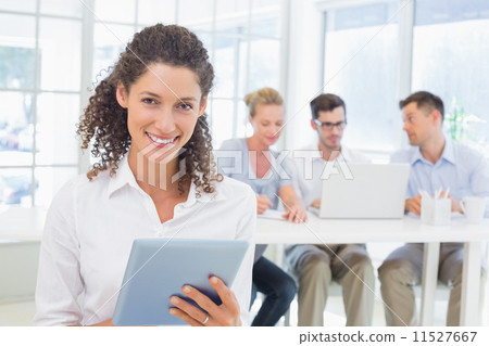Casual businesswoman using tablet with team behind her Casual businesswoman using tablet with team behind her 11527667
