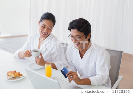 Couple in bathrobes shopping online in the morning 11528395