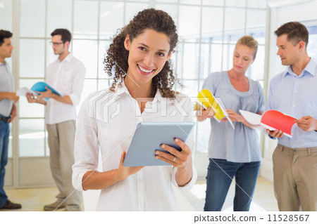 Casual businesswoman using tablet with team behind her Casual businesswoman using tablet with team behind her 11528567