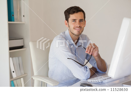 Casual businessman smiling at camera at his desk 11528630