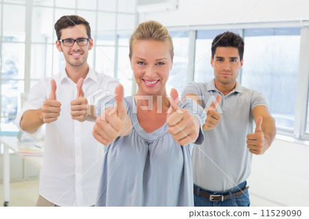 Casual business team smiling at camera with thumbs up Casual business team smiling at camera with thumbs up 11529090