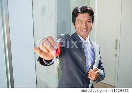 Confident estate agent standing at front door showing key Confident estate agent standing at front door showing key 11529372