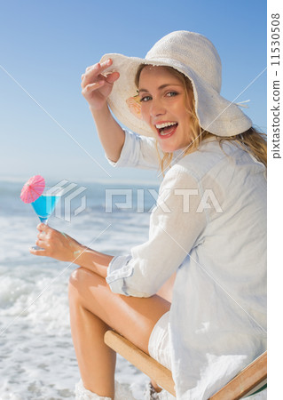 Smiling blonde relaxing in deck chair by the sea holding cocktai Smiling blonde relaxing in deck chair by the sea holding cocktai 11530508