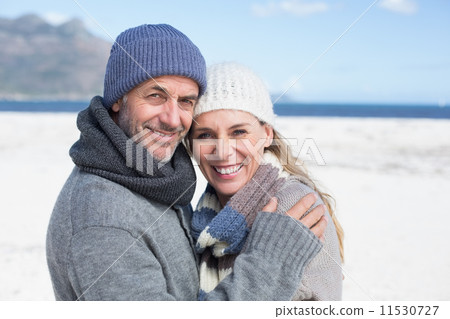 Attractive couple smiling at camera on the beach in warm clothin 11530727