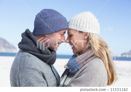 Attractive couple smiling at each other on the beach in warm clo Attractive couple smiling at each other on the beach in warm clo 11531182