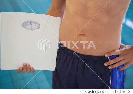 Fit man in swimming trunks standing by the pool holding weighing 11531660