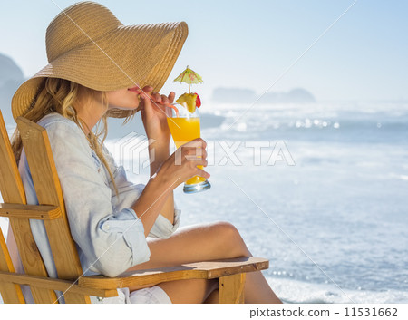 Smiling blonde relaxing in deck chair by the sea sipping cocktai Smiling blonde relaxing in deck chair by the sea sipping cocktai 11531662